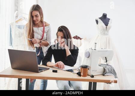 Guardando sul laptop. Due donne designer di moda lavora sui nuovi vestiti in officina Foto Stock