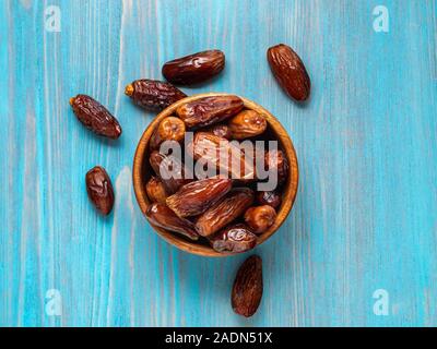 Frutti di data palm, frutta secca nella ciotola di legno. Cibi tradizionali del Medio Oriente e del Nord Africa. Vista superiore, luminoso blu sullo sfondo di legno. Foto Stock