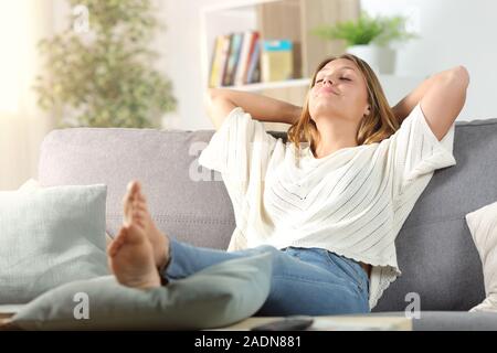 Spensierata rilassante donna seduta su un divano nel soggiorno di casa Foto Stock