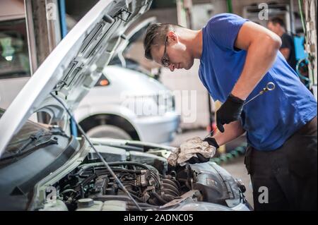 Auto riparatore meccanico di controllare il livello di olio nel motore di auto, sotto il cofano del veicolo service shop Foto Stock