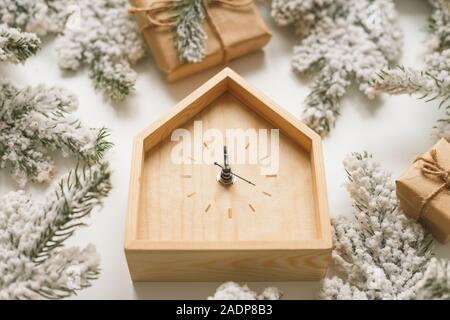 Natale e Anno nuovo ancora in vita. Orologio in legno mostra cinque minuti a mezzanotte. Rami di abete e scatole intorno a. Vista da sopra Foto Stock