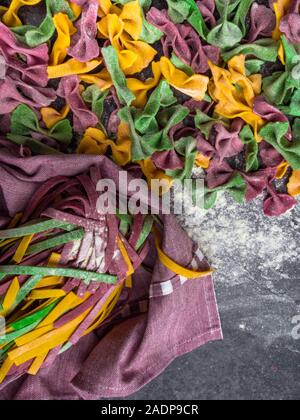 Varietà di pasta cruda, tipi di farfalle bow tie-, fettuccine o tagliatelle pasta colorata su uno sfondo grigio con farina Foto Stock