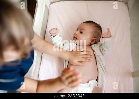 Big Sister di toccare la pelle di un neonato i gemelli con disabilità nel presepe Foto Stock