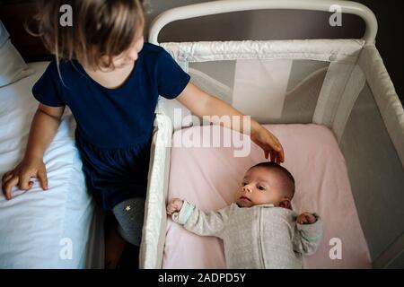 4 anni di toccare la testa di un neonato sorella nel presepe con foglio rosa Foto Stock