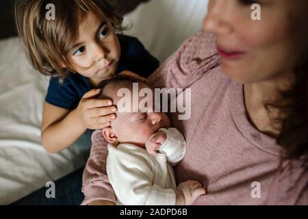 4 anni di toccare la testa del neonato a pelo essendo tenuto dalla madre Foto Stock
