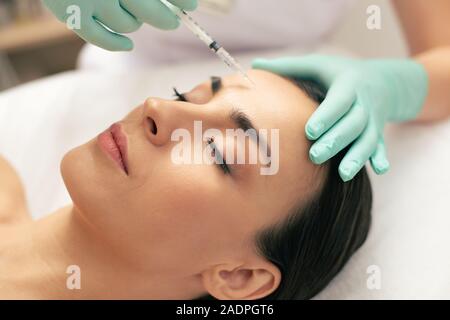 Volto di donna calma e mano rendendo iniezione in fronte Foto Stock