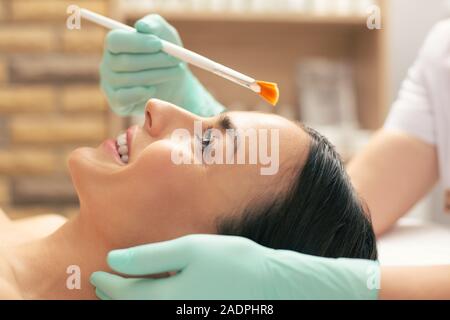 Vista laterale della donna il viso e le mani nel guanto di gomma holding spazzola peeling Foto Stock