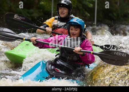 Maschi e femmine di kayakers Shooting the Rapids presso il National White Water centro sul fiume Tryweryn nel Parco Nazionale di Snowdonia Foto Stock