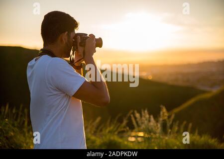 Un uomo prende una fotografia con la sua macchina fotografica Nikon durante un tramonto sulla vetta del Monte Wellington di Auckland, in Nuova Zelanda. Foto Stock
