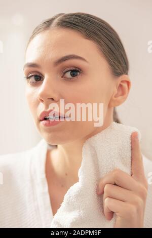 Attenta donna che guarda curioso mentre in piedi con asciugamano Foto Stock
