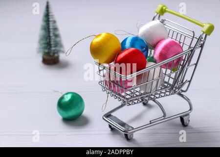 Carrello della spesa e colorato nuovo anno palle su sfondo bianco, l'albero di Natale, piatto shopping laici, spazio di copia Foto Stock