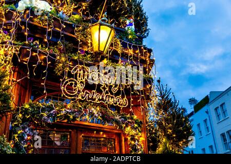 Buon Natale e opulente luci e decorazioni natalizie sulla facciata del Churchill Arms Pub, Londra, Regno Unito Foto Stock