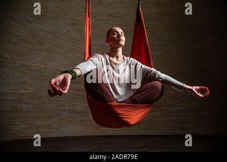 Bella donna rilassante mentre medita durante lo yoga dell'antenna Foto Stock