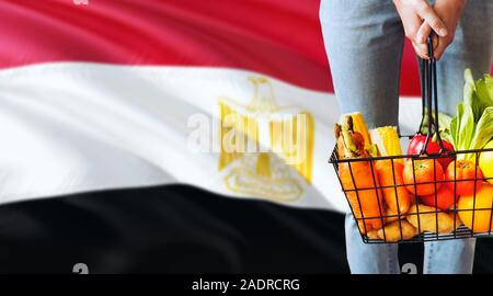 La donna è in possesso di un supermercato cestello, Egitto sventola bandiera dello sfondo. Il concetto di economia per la frutta e la verdura fresca. Foto Stock