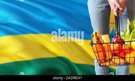 La donna è in possesso di un supermercato cestello, Ruanda sventola bandiera dello sfondo. Il concetto di economia per la frutta e la verdura fresca. Foto Stock