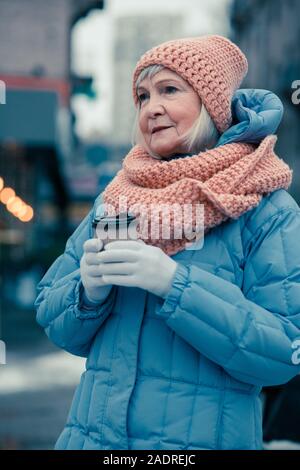 Premurosa donna età tenendo tazza di caffè all'aperto Foto Stock