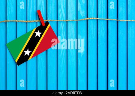 Bandiera di Saint Kitts e Nevis appesi stendibiancheria attaccato con clothespins in legno su aqua blu sullo sfondo di legno. Giornata nazionale del concetto. Foto Stock
