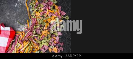 Varietà di pasta cruda, tipi di farfalle bow tie-, fettuccine o tagliatelle pasta colorata su uno sfondo grigio con farina Foto Stock