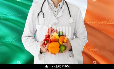 Medico è in possesso di frutta e verdura in mani con Irlanda bandiera dello sfondo. Sistema sanitario nazionale concetto, tema medico. Foto Stock