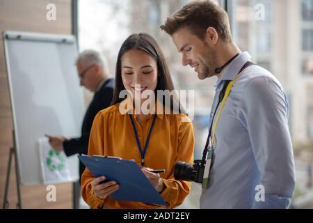 Donna dai capelli scuri che mostra reporter note al suo collega Foto Stock