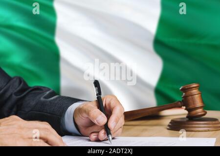 Giudicare la scrittura su carta in aula con la Nigeria bandiera dello sfondo. Martello di legno di uguaglianza il tema e il concetto giuridico. Foto Stock