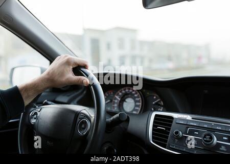 Maschio di mano sul volante nero alla guida di una vettura il pendolarismo per il lavoro Foto Stock