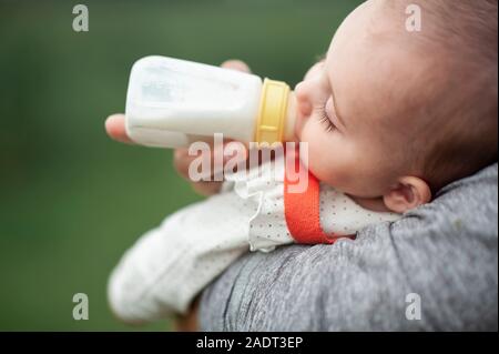Baby girl dormendo mentre bere una bottiglia all'aperto Foto Stock