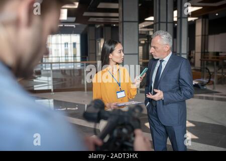 Asian reporter femmina parlando di un famoso uomo d affari Foto Stock