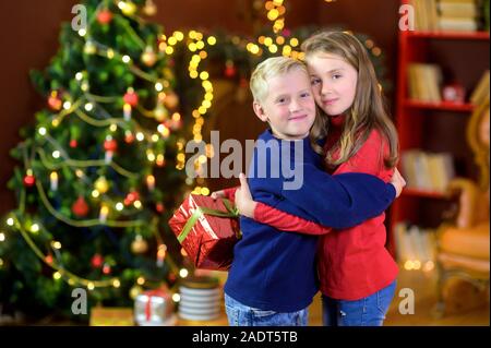 Dei bambini felici dare doni mentre in una stanza sullo sfondo di un albero di festa. Abbraccio e sorriso. Natale e Anno Nuovo Foto Stock