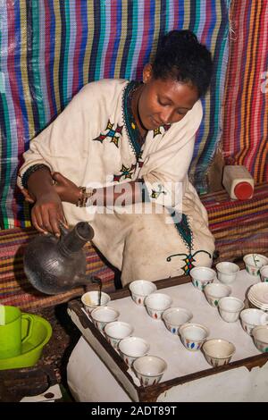 Etiopia, Amhara Region, Bahir Dar, Lago Tana Zege Penisola, caffè femmina venditore versando buna nero caffè Foto Stock