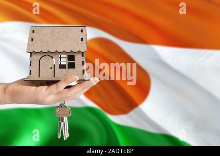 Donna mano azienda casa in legno e le chiavi a portata di mano. Niger bandiera con il concetto di affitto, acquisto, assicurazioni, edilizia immobiliare, eco house. Foto Stock