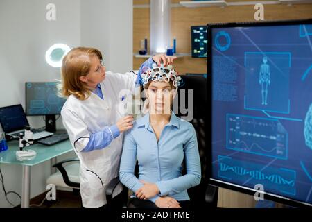 Medico di neurologia adattamento casco durante un cervello procedura di scansione. Laboratorio moderno Foto Stock