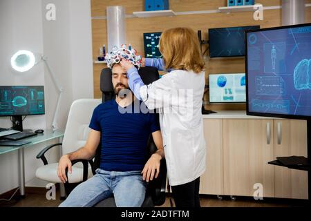 Medico mettendo brainwaves auricolare di scansione sul paziente di sesso maschile. Laboratorio di neurologia e dispositivo di scansione Foto Stock