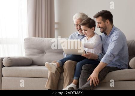 Nonno, figlio e nipote utilizzando laptop seduto sul divano in ambienti interni Foto Stock