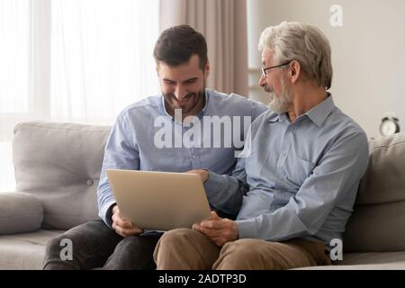 Padre e cresciuto figlio siedono insieme sul lettino con il computer portatile Foto Stock