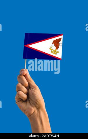 Donna mano azienda Samoa Americane bandiera con bastone, sventola bandiera sul profondo blu del cielo. Tema nazionale, profondo cielo blu. Foto Stock