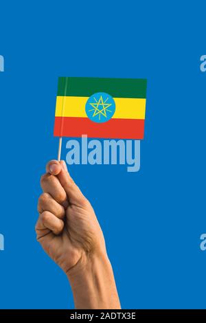 Donna mano azienda Etiopia bandiera con bastone, sventola bandiera sul profondo blu del cielo. Tema nazionale, profondo cielo blu. Foto Stock