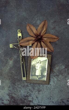 Essiccato brown fiore di Clematis Hagley ibrido su metallo opacizzato con foto incorniciate degli anni cinquanta la donna nel giardino e del crocifisso Foto Stock