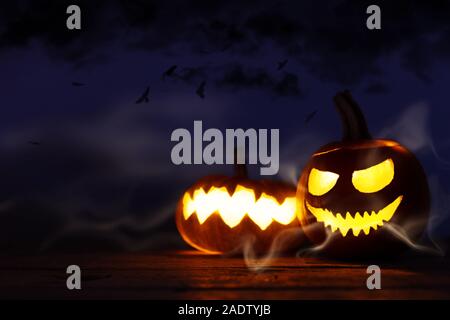 Decorazione Halloween su uno sfondo di legno intagliato, zucche con scary smorfie e la luce nella parte anteriore del cielo notturno, copiare lo spazio per testo per feste a tema Foto Stock