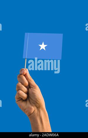 Donna mano che tiene la Somalia bandiera con bastone, sventola bandiera sul profondo blu del cielo. Tema nazionale, profondo cielo blu. Foto Stock