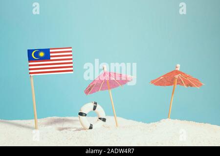 Bandiera in miniatura della Malesia sulla spiaggia con ombrelloni colorati e salvagente. Concetto di viaggio, Tema estivo. Foto Stock