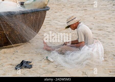 Pescatore vietnamita rammendo rete da pesca e bamboo carrello barca Hoi An Vietnam Foto Stock
