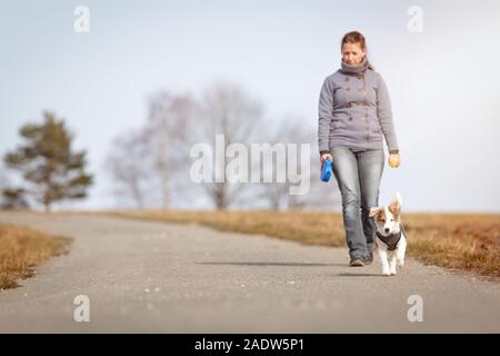 La donna sta facendo una passeggiata con il suo cucciolo di cane, mentre il PET è mantenuto su un gioco Foto Stock