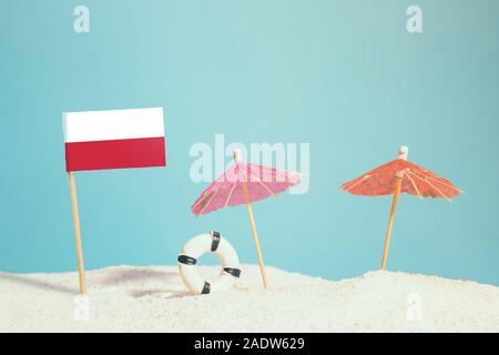 Miniatura bandiera della Polonia sulla spiaggia con ombrelloni colorati e salvagente. Concetto di viaggio, Tema estivo. Foto Stock