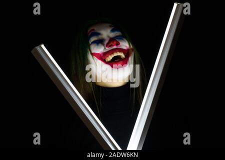 Ragazza con un trucco da clown ride follemente su sfondo scuro. Foto Stock