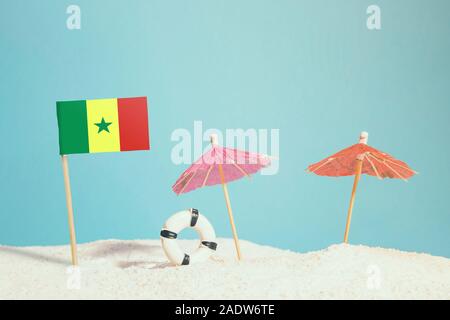 Bandiera in miniatura del Senegal sulla spiaggia con ombrelloni colorati e salvagente. Concetto di viaggio, Tema estivo. Foto Stock