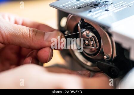 La mano di un uomo è la filettatura di un filo al piedino della sua macchina da cucire Foto Stock