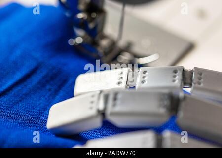 Produzione industriale di massa di vestiti in un tessuto tessile, primo piano di una mano di robot utilizzando una macchina di cucitura Foto Stock