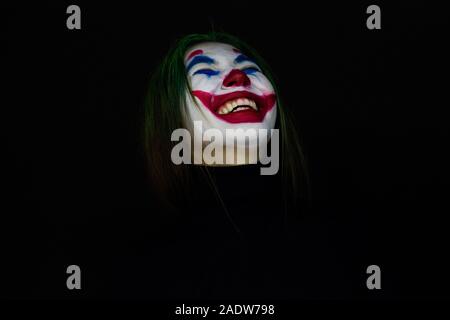 Ragazza con un trucco da clown ride follemente su sfondo scuro. Foto Stock