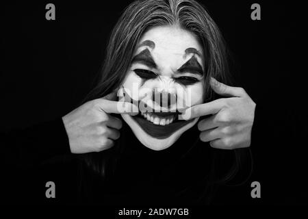 Ragazza con un trucco da clown ride follemente su sfondo scuro. Foto Stock